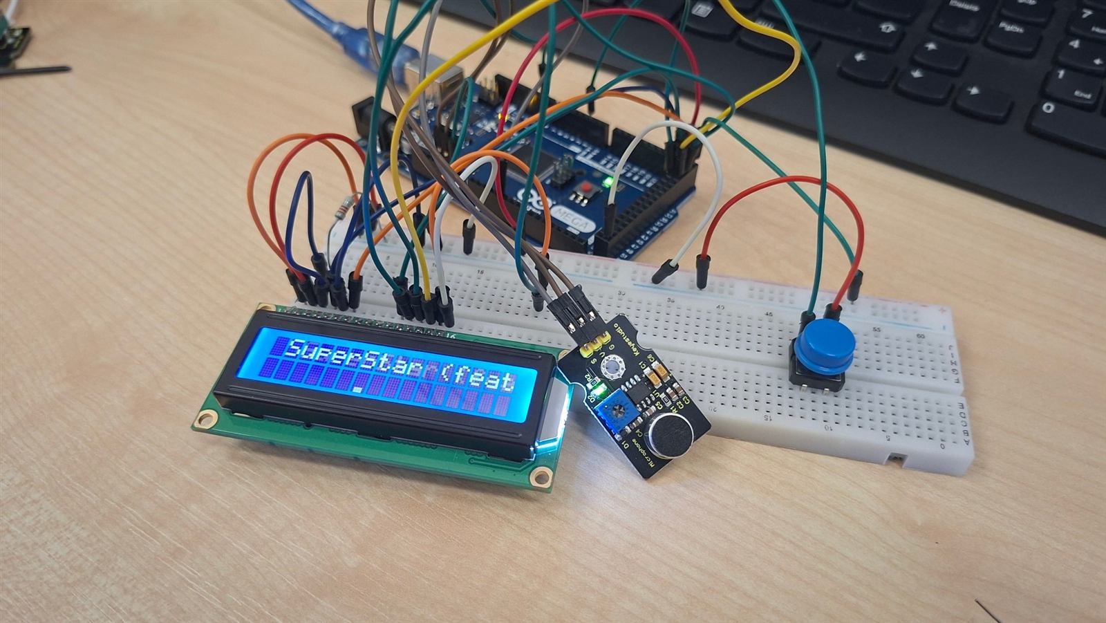 Arduino Mega s LCD displejom, zvukovým senzorom a tlačidlom. Na displeji sa posúva názov skladby SuperStar